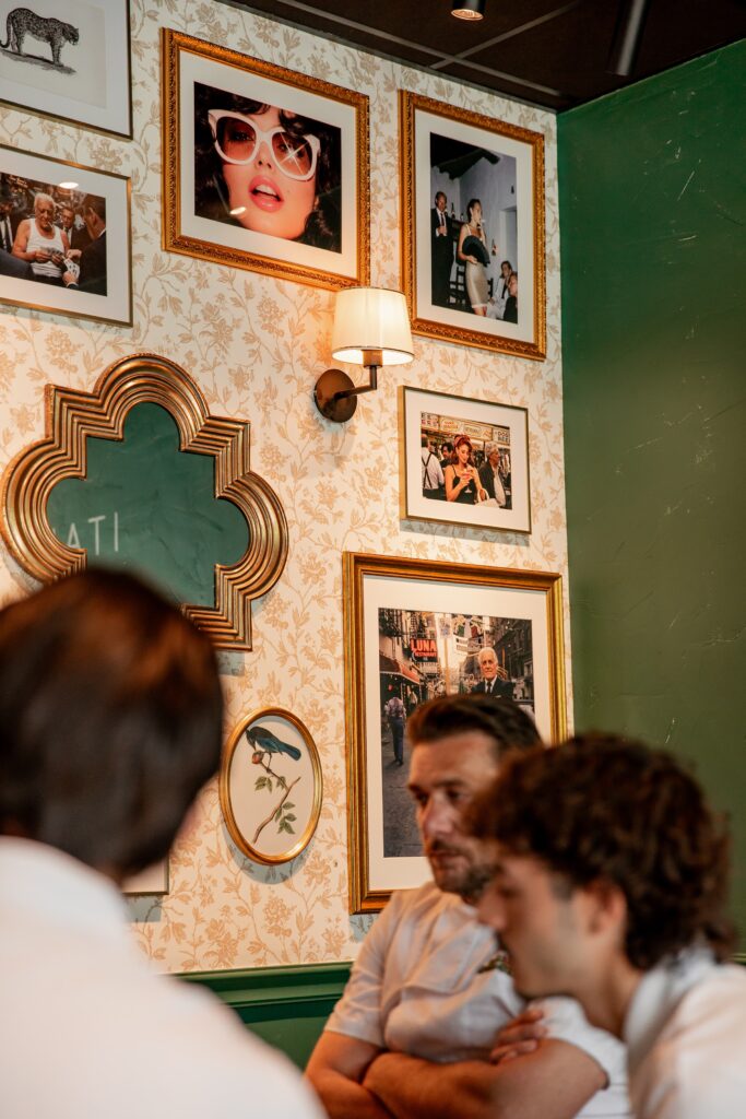 Des clients attablés devant le mur de cadres et le papier peint fleuri d'Italian Queen Meylan