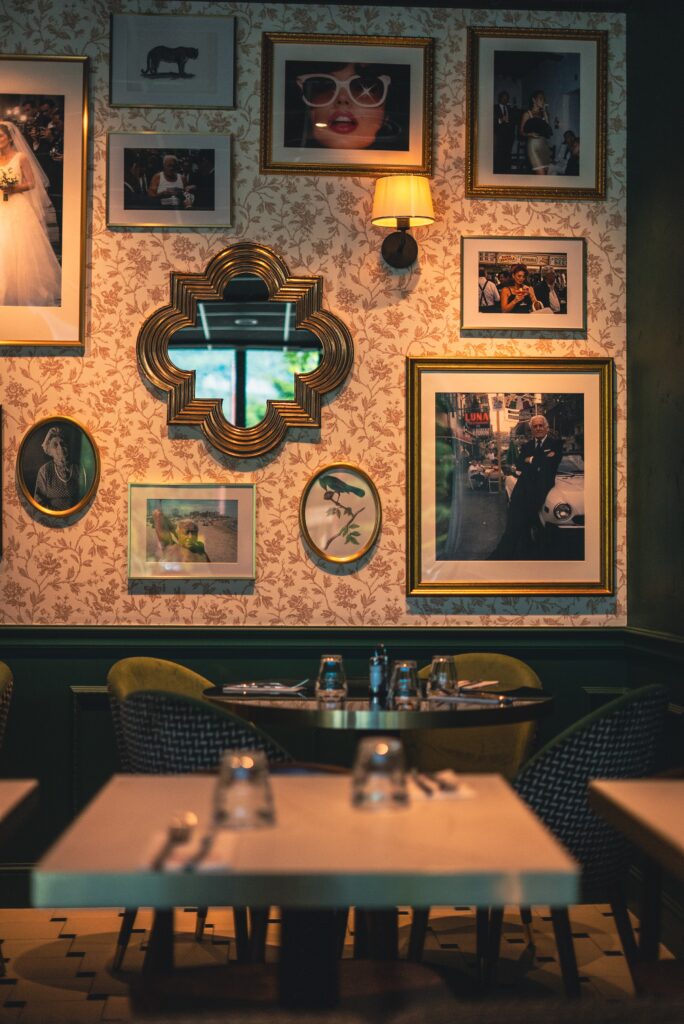 Le miroir doré en arabesque entouré de photos encadrées, sur le papier peint fleuri de la salle d'Italian Queen Meylan